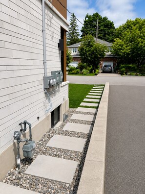 A residential street with a house featuring a white exterior, a driveway, and a stone pathway leading to the garage.
