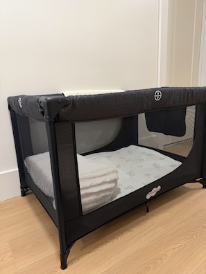 A portable baby playpen with a mesh top and side panels, featuring a handle and wheels for mobility.