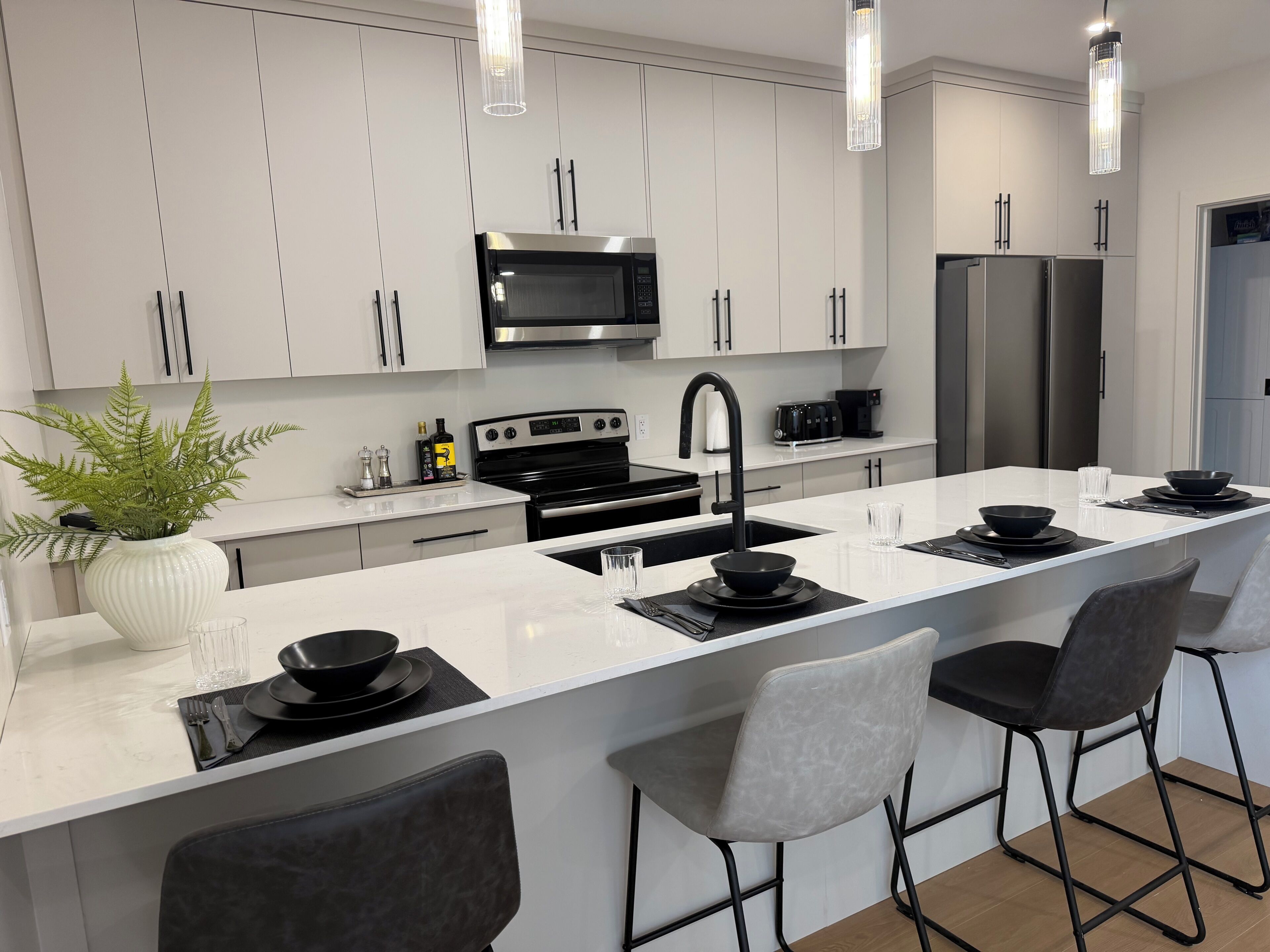 A modern kitchen with white cabinetry, stainless steel appliances, a central island with seating, and pendant lighting.