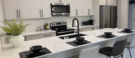 A modern kitchen with white cabinetry, stainless steel appliances, a central island with seating, and pendant lighting.