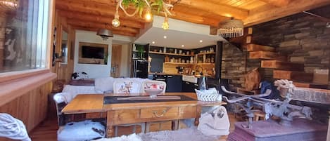 A cozy cabin interior with a wooden dining table, a fireplace, and a kitchen area.