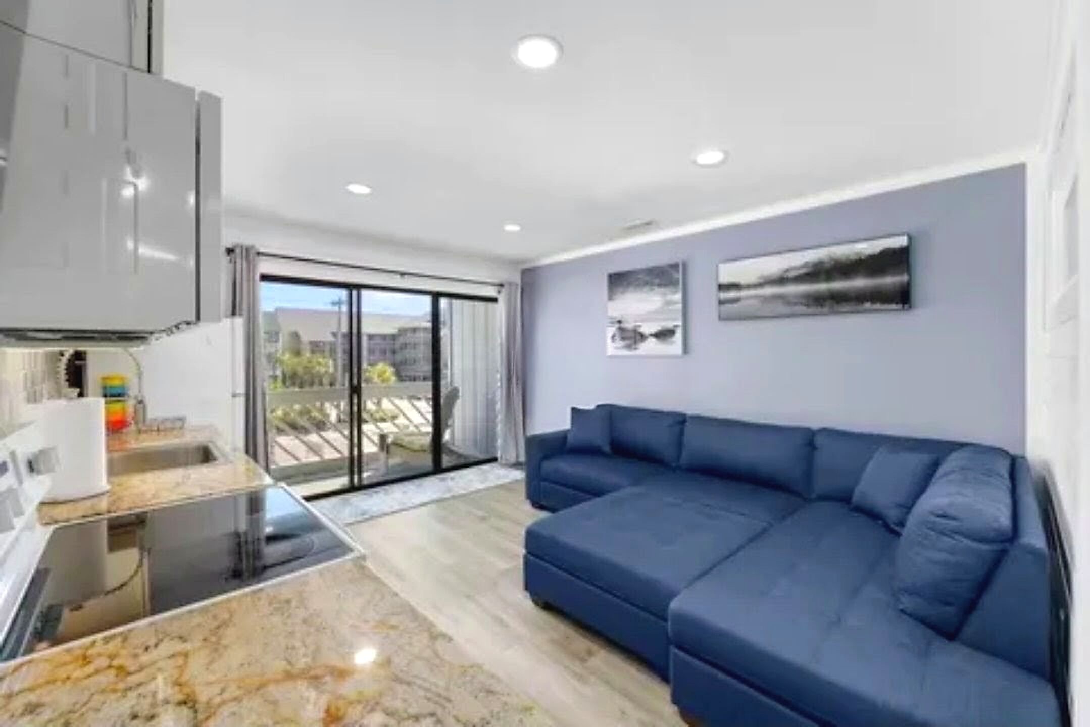 A modern living space with a kitchen, a blue sofa, and a balcony with a view.
