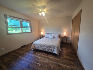 A bedroom with a bed, two bedside lamps, a ceiling fan, a window, and a wooden wardrobe.