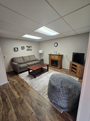 Ein Wohnzimmer mit Sofa, Couchtisch, Hocker, Kamin, TV-Schrank und einer Wanduhr.