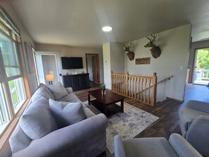 A living room with a sofa, a coffee table, and a TV. There is a staircase with wooden railings and a sign above it. - Your Rockton Retreat in the Heart of Kickapoo Valley between Ontario and LaFarge (La Farge)