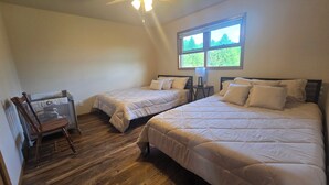 Un dormitorio con dos camas, piso de madera, ventilador de techo y ventana con vista.