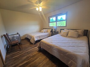 Ein Schlafzimmer mit zwei Betten, Holzboden, Deckenventilator und einem Fenster mit Blick.