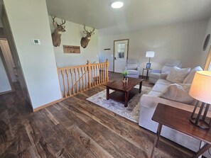 Ein Wohnzimmer mit Holzboden, einer Couch, einem Couchtisch und zwei an der Wand aufgehängten Hirschköpfen.