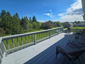 A wooden deck with a white railing, a round table with chairs, and a view of a green landscape with trees and a barn. - Your Rockton Retreat in the Heart of Kickapoo Valley between Ontario and LaFarge (La Farge)