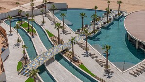 A large, multi-level swimming pool with palm trees and lounge chairs. - 3-bedroom luxury beachfront condo - Encantame Soleil with lazy river, waterslide (Puerto Penasco, Son)