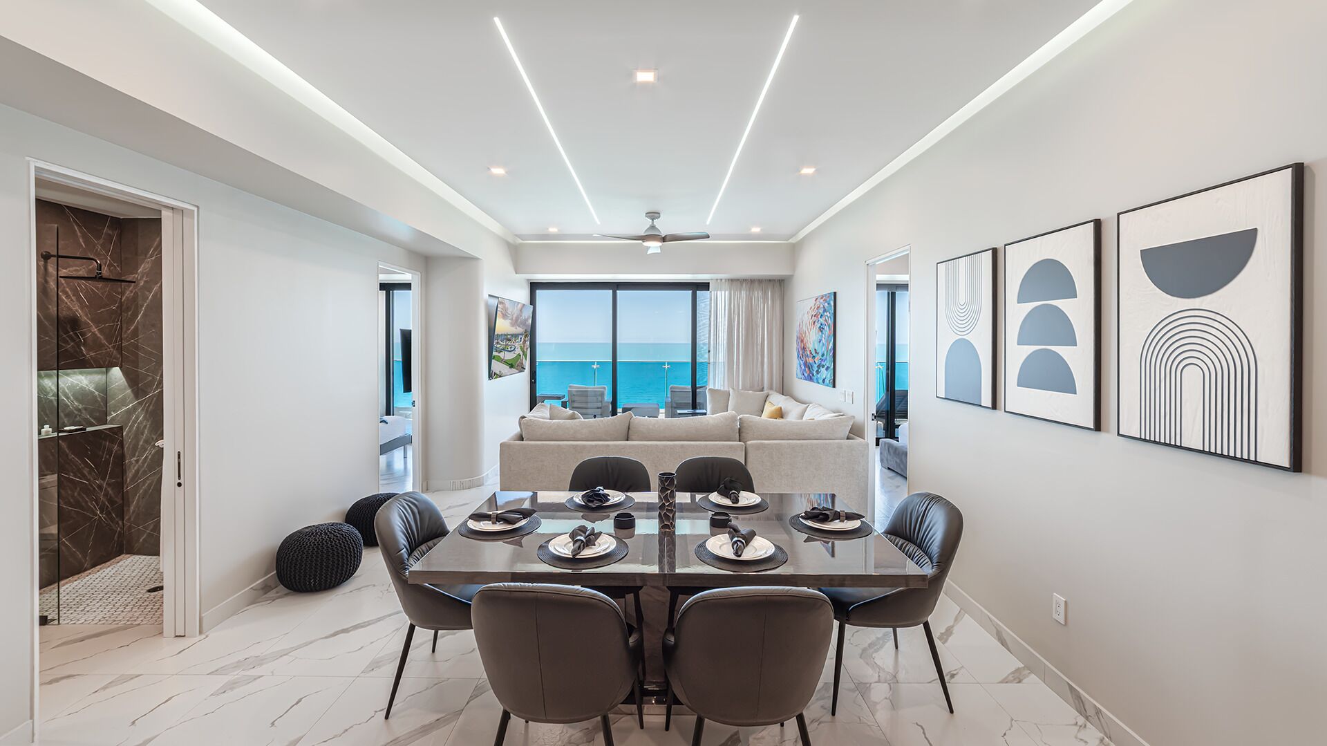 Un espace repas moderne avec vue sur la mer, un ensemble de canapés et des œuvres d’art accrochées aux murs.