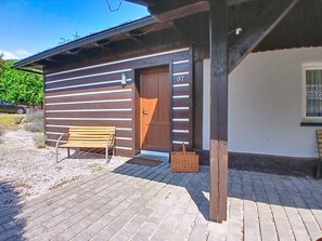 Ein Holzbau mit einer Tür, auf der '97' steht, und einer Bank davor.