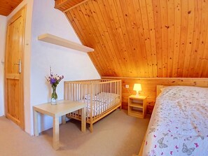 A room with a sloped ceiling, a crib, a bedside table with a lamp, and a bed with a patterned bedspread. - Černý Důl by Interhome (Cerny Dul)