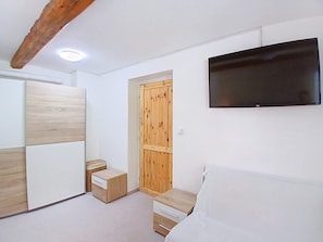 A bedroom with a bed, a TV mounted on the wall, a wooden wardrobe, and a small bedside table. - Černý Důl by Interhome (Cerny Dul)