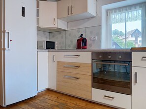 A kitchen with white cabinets, a microwave, a red kettle, and an oven. - Černý Důl by Interhome (Cerny Dul)