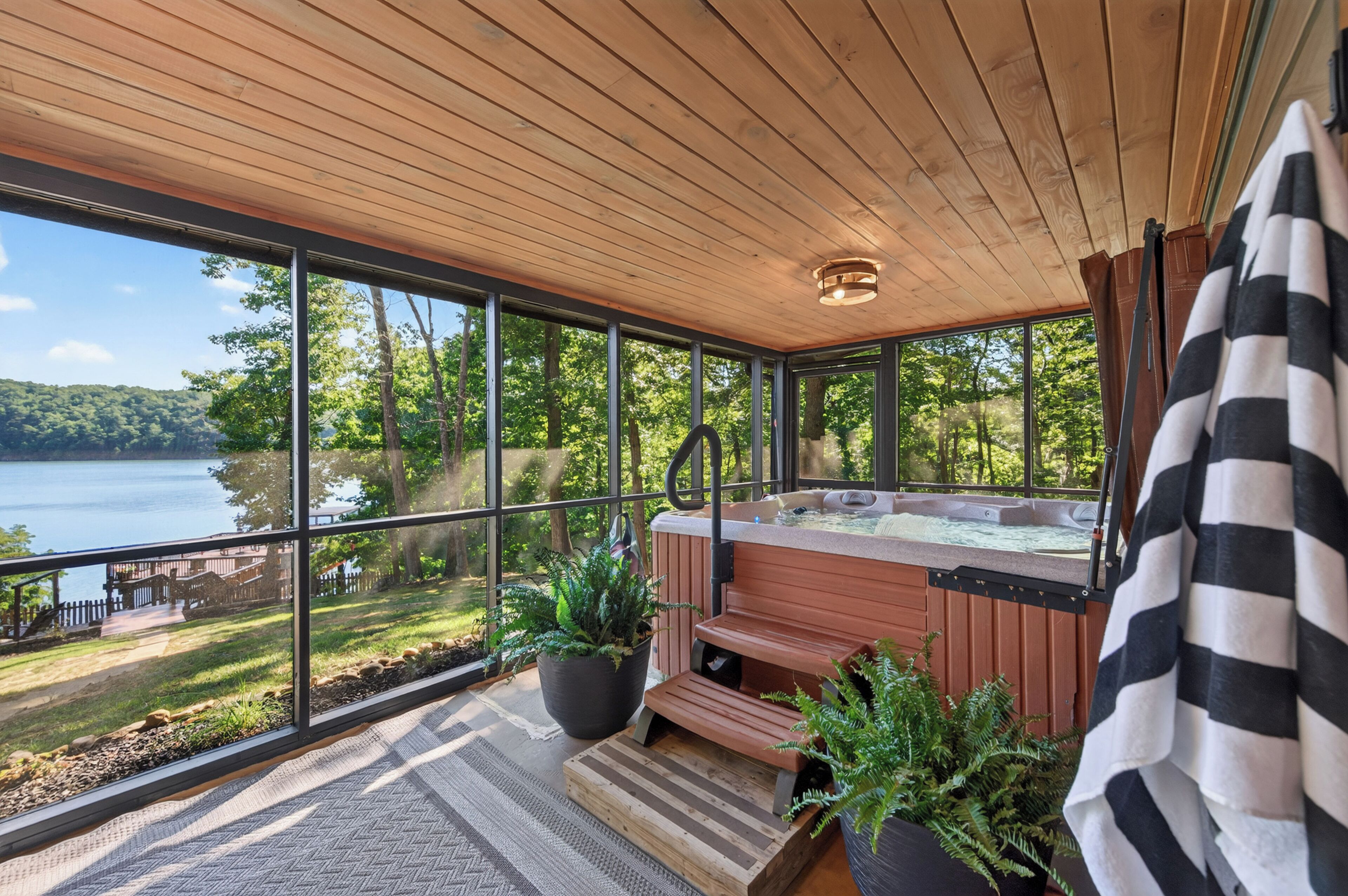 A hot tub on a wooden deck with large windows overlooking a lake.