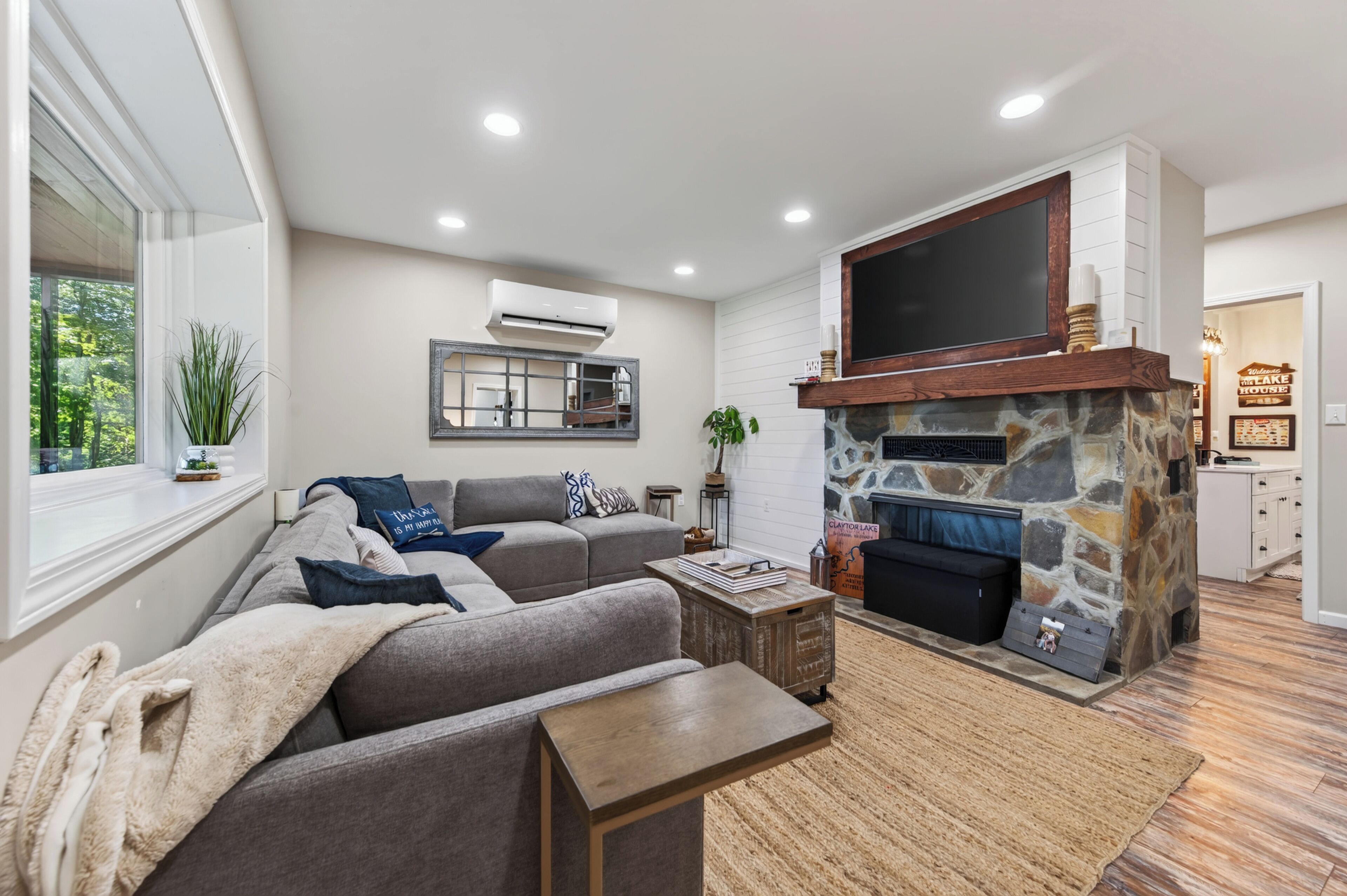 A modern living room with a stone fireplace, a large flat-screen TV mounted above it, and a cozy seating area with a sofa and a coffee table.