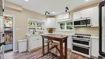 A modern kitchen with white cabinetry, a wooden dining table, and a built-in oven.