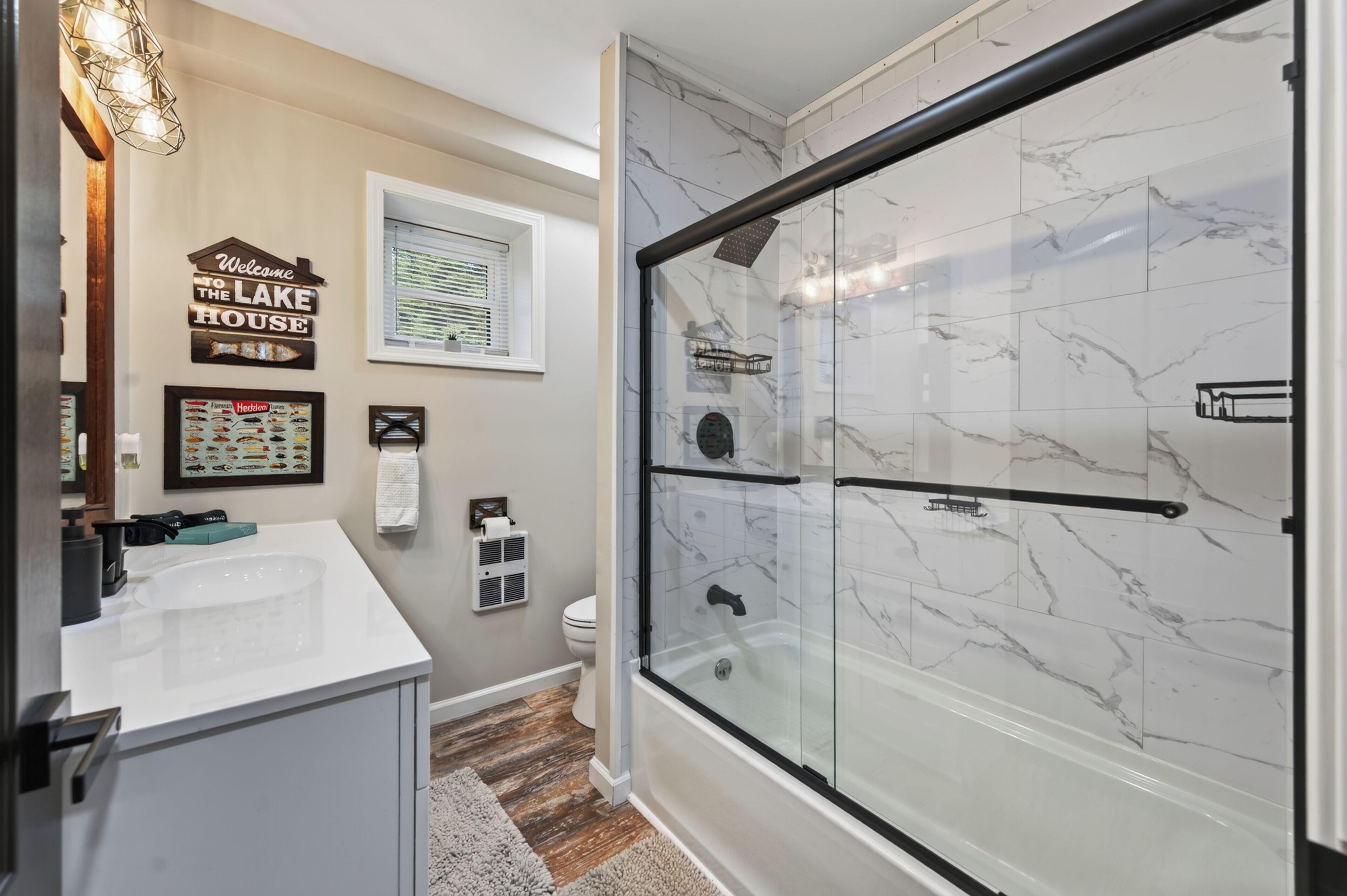 A bathroom with a glass shower enclosure, a sink, a toilet, and a framed menu on the wall.