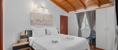 Un dormitorio con techo de madera, una cama con ropa de cama blanca, un cuadro en la pared y una ventana con cortinas.