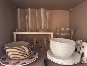 Ein Lagerbereich mit klarem Glasgeschirr und Tellern, manche mit Henkeln, andere ohne, an Regalen und einem Tisch angeordnet.