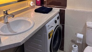 A compact bathroom with a sink, mirror, washing machine, and toilet. - Klara Florenza (Hurghada)