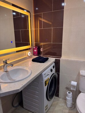 Ein kleines Badezimmer mit Waschbecken, Spiegel, Waschmaschine und Toilette.