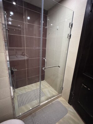 A glass-enclosed shower stall with a handrail, a tiled floor, and a small mat at the entrance. - Klara Florenza (Hurghada)