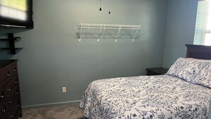 Ein Schlafzimmer mit Bett, Kommode, Fernseher und einer Wandablage.