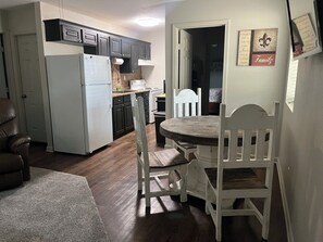 A compact kitchen with a refrigerator, stove, and cabinets. There is a dining table with chairs and a rug in the foreground. - Cozy 2-bedroom Home in serene Gloster with cool AC and privacy (Gloster)