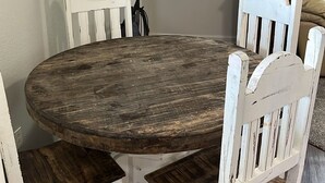 Ein Essbereich mit einem runden Holztisch und weißen Stühlen. Ein Flachbildfernseher ist an der Wand oberhalb des Tisches angebracht.