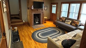 Una sala de estar con chimenea, un sofá, un televisor y una ventana.