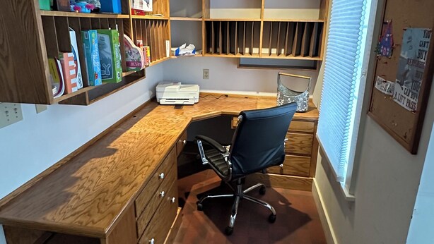 Un despacho en casa con escritorio, silla, estanterías y ventana.