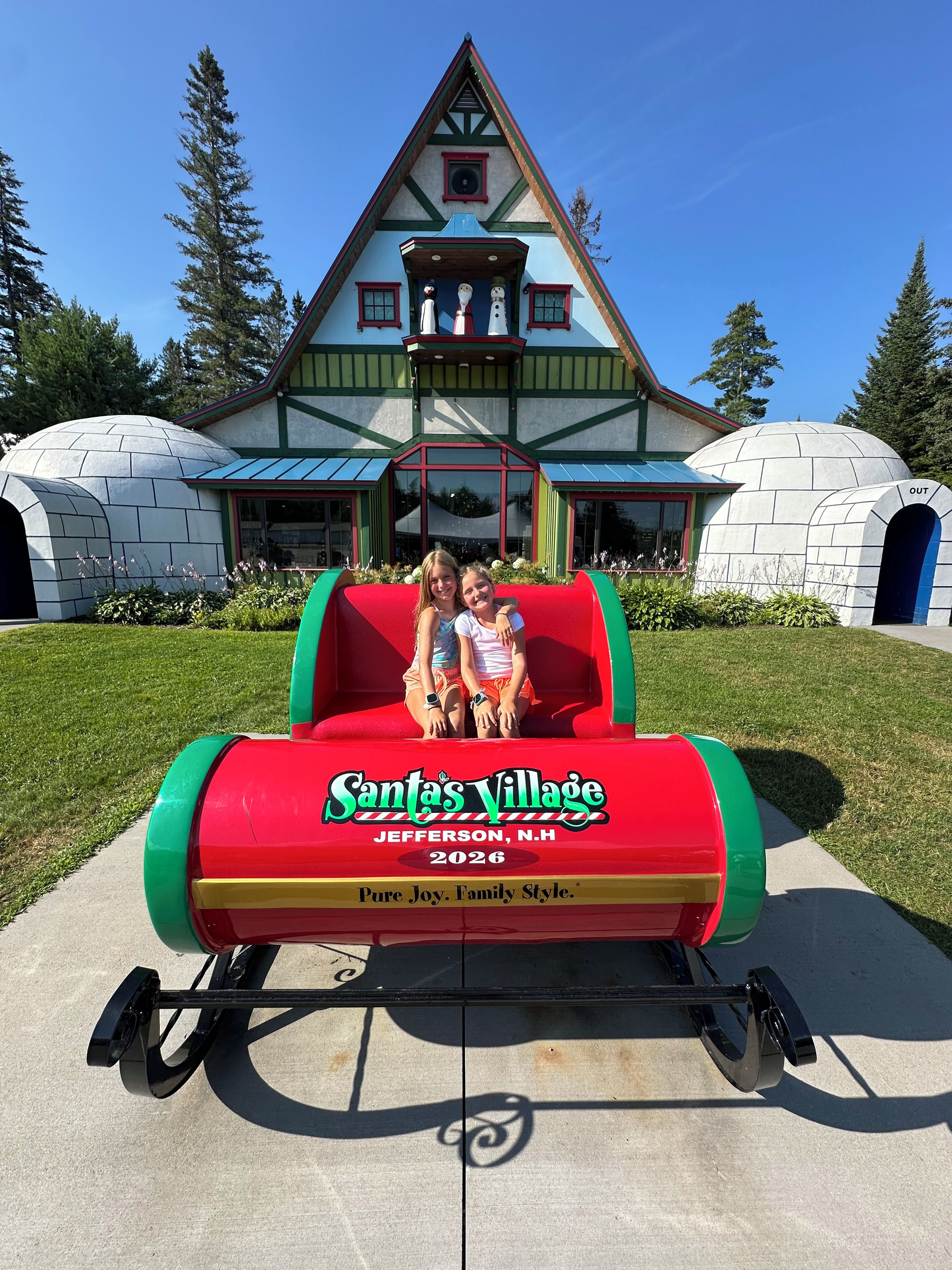 A red and green Santa's Village ride with two children seated.