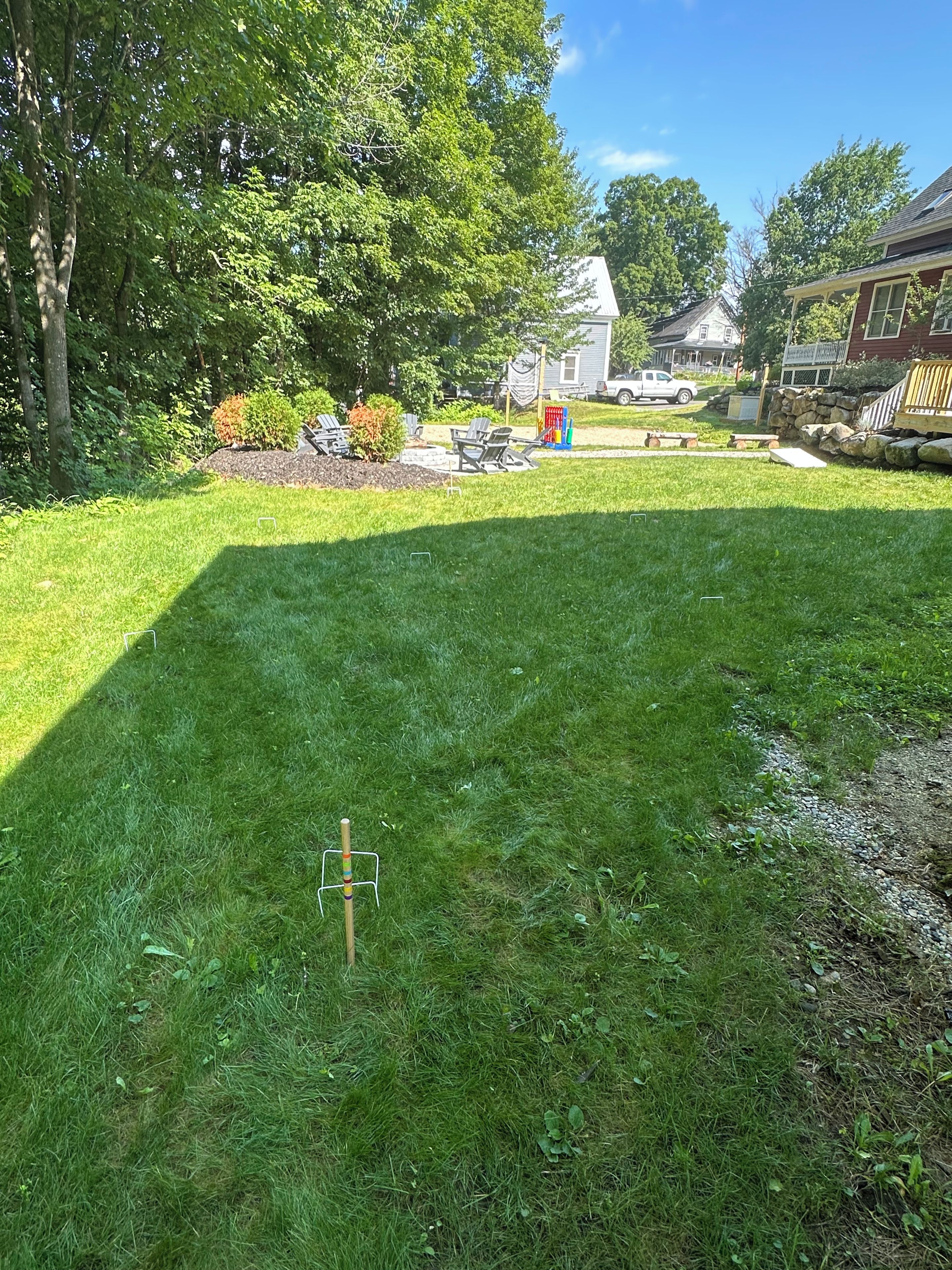 A well-maintained grassy yard with a wooden swing set, a stone wall, and a house in the background.