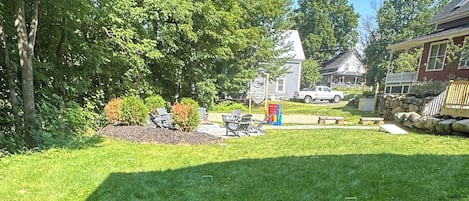 A well-maintained grassy yard with a wooden swing set, a stone wall, and a house in the background.