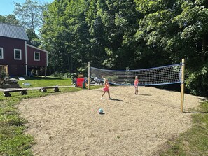 Ein Volleyballfeld mit Netz, umgeben von Bäumen und einem Haus.