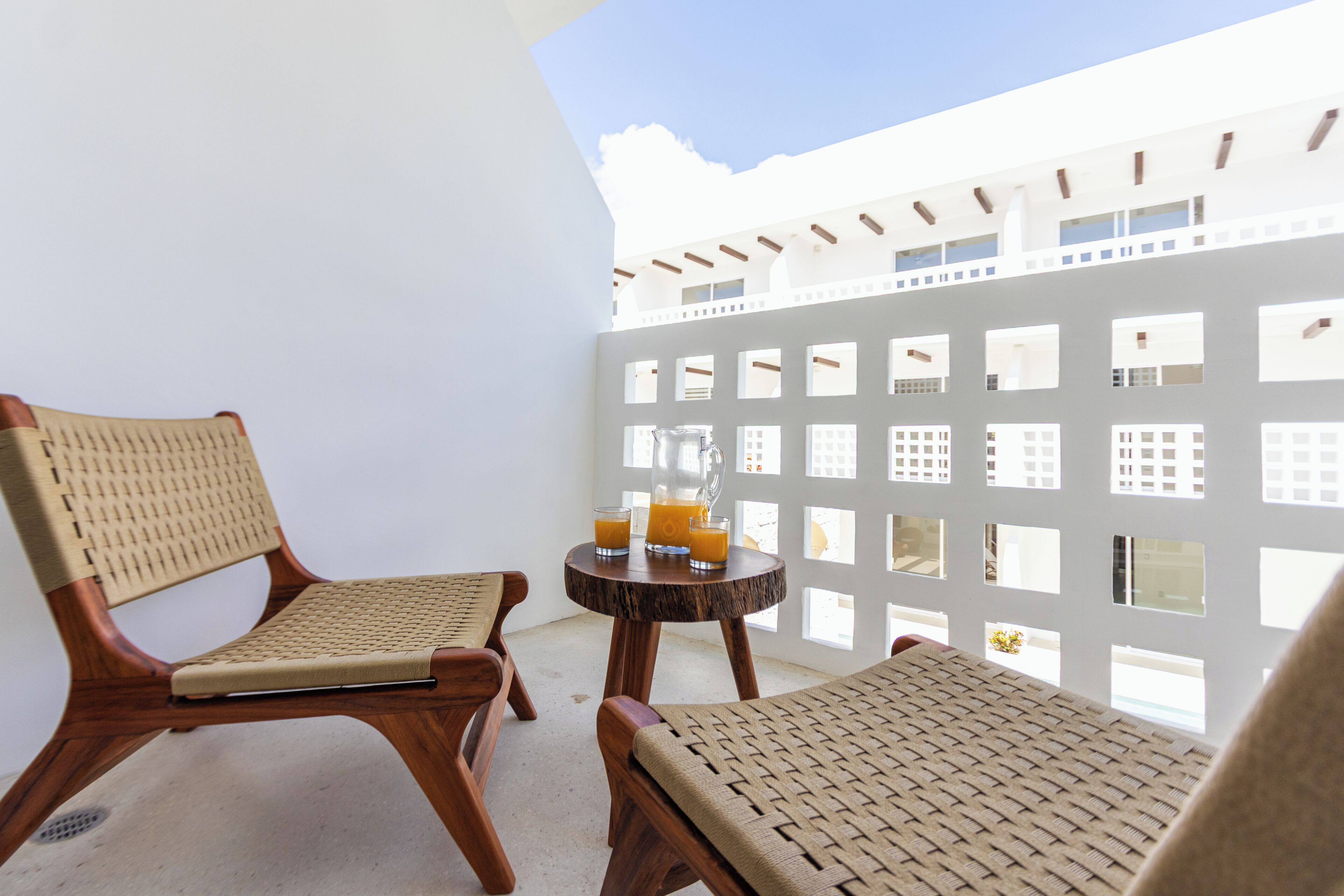 Ein Balkon mit zwei Korbstühlen, einem kleinen runden Tisch und einem weißen Trennwerk mit Fenstern.