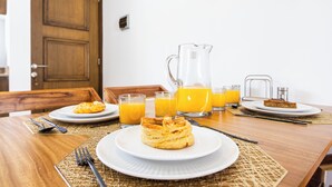 En morgenmadsopstilling med tallerkener med kager, glas med appelsinjuice og en kande juice på et træbord.