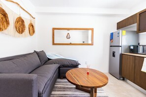 A modern living room with a grey sofa, a wooden coffee table, and a kitchen area with a refrigerator and microwave. - Nature, Tranquility, and the Beach (Tulum)
