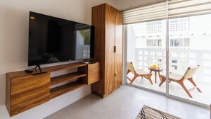 En moderne stue med et fladskærms-TV monteret på en trækommode, samt en skydedør, der fører ud til en balkon med udendørs møbler.