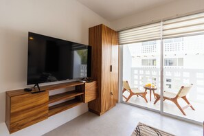 A modern living room with a flat-screen TV mounted on a wooden console, a sliding glass door leading to a balcony with outdoor seating. - Nature, Tranquility, and the Beach (Tulum)