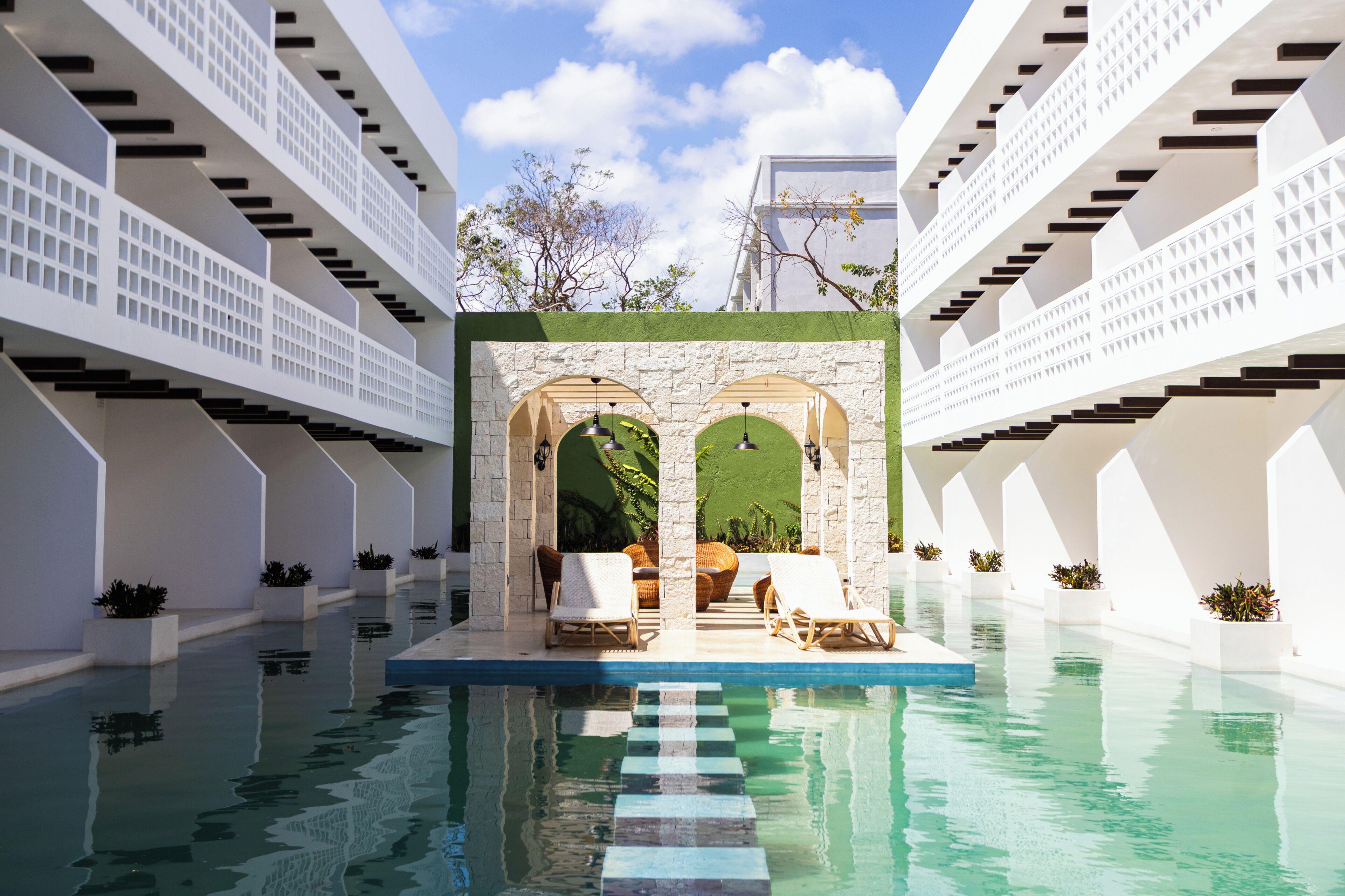 Zona de piscina con un arco central, sillas de descanso y cielo despejado.