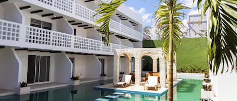 Uma área de piscina moderna com água azul cristalina, arquitetura branca e mobiliário de exterior.