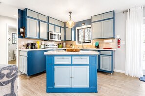 A modern kitchen with blue cabinetry, a central island, and a hanging light fixture. - Pocono Pines Retreat Hot Tub & Cozy Escape in PCP (Tobyhanna)