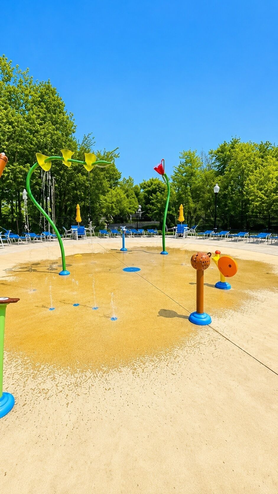 Un espace de jeux aquatiques avec plusieurs fontaines et un coin salon équipé de chaises bleues.