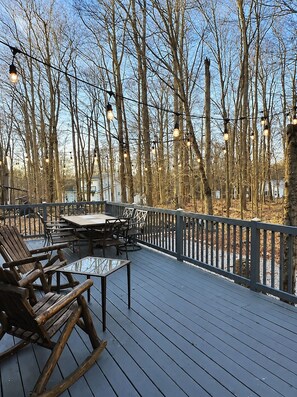 An outdoor deck with a table and chairs, surrounded by a railing and trees. - Pocono Pines Retreat Hot Tub & Cozy Escape in PCP (Tobyhanna)