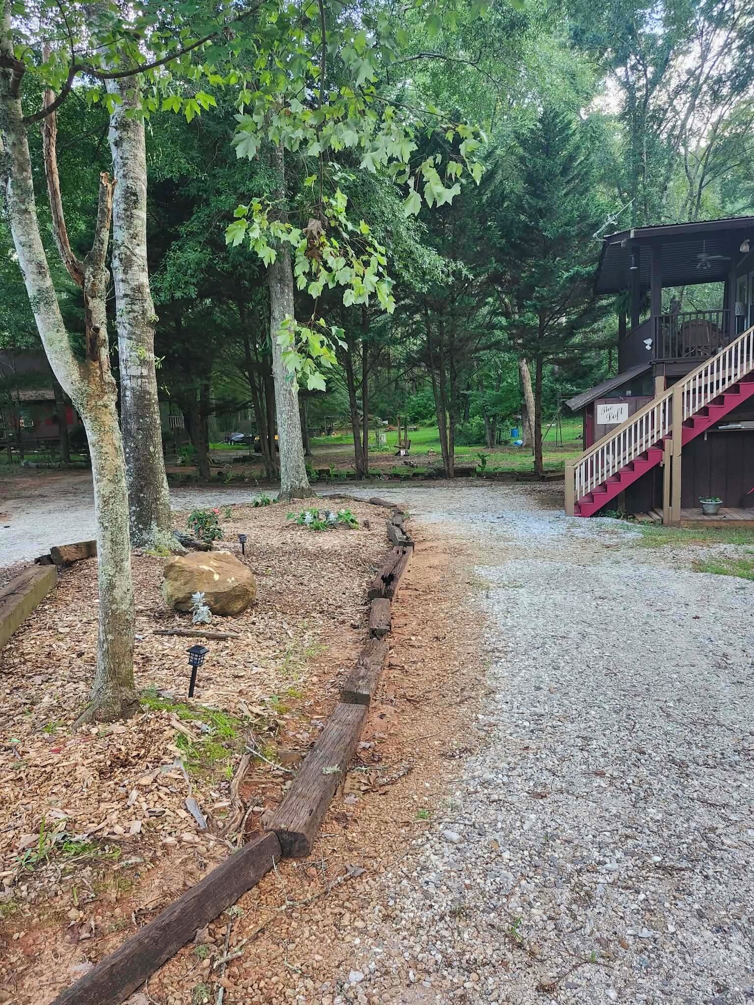 Ein Kiesweg führt zu einer Holzhütte mit einer roten Treppe.