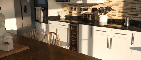 Una cocina moderna con armarios blancos, una mesa de comedor de madera y un revoque de ladrillo.