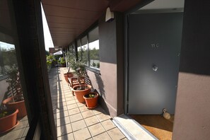 Ein Balkon mit Blumentöpfen, eine Tür mit der Aufschrift '11 C' und Blick zum Himmel.